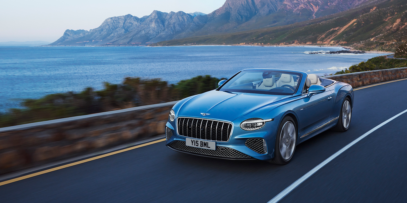 Bentley Monaco New Bentley Continental GTC Azure convertible in Light Windsor blue paint with 22 inch Azure wheels and chrome grill, driving dynamically by the sea