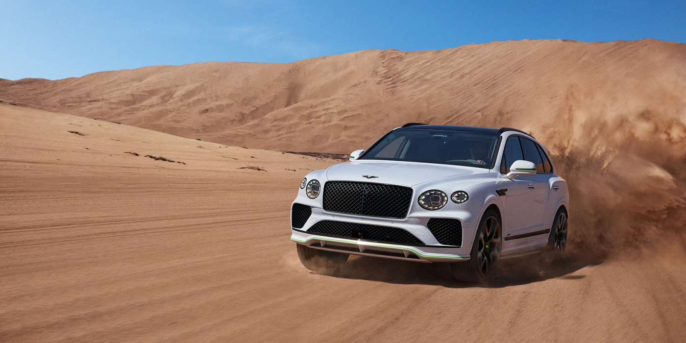 Bentley Monaco Bentley Bentayga Speed SUV front three quarter in Snow Quarts Pearlescent by Mulliner white paint driving dynamically through the desert
