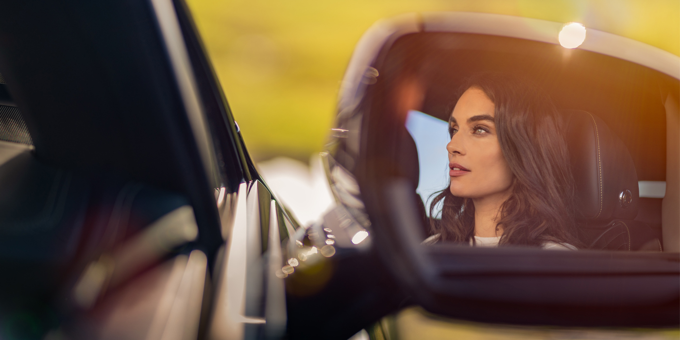 Bentley Monaco profile of dark haired woman's face in mirror of Bentley car in sunlight