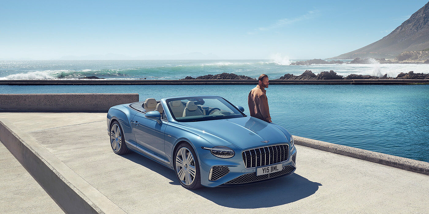 Bentley Monaco New Bentley Continental GTC Azure convertible front view in Light Windsor blue paint with 22 inch ten spoke wheels parked by the sea in the sunshine