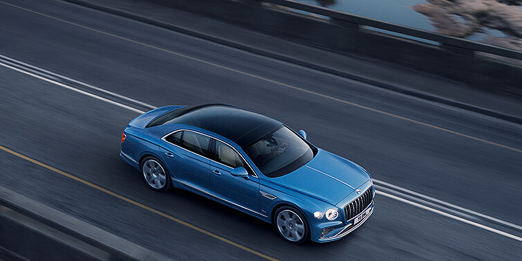 Bentley Monaco New Bentley Flying Spur Azure sedan in Light windsor blue paint by Mulliner, with 22 inch Azure wheels seen from overhead driving dynamically on a country road