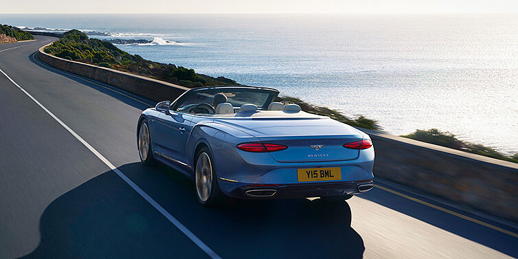 Bentley Monaco New Bentley Continental GTC Azure convertible rear view in Light Windsor blue paint with 22 inch ten spoke wheels driving dynamically on an ocean road in the sunshine