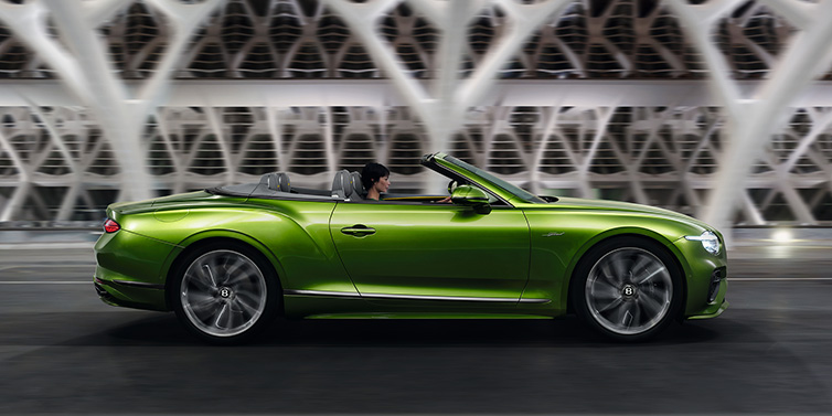 Bentley Monaco Bentley Continental GTC Speed convertible side profile in Tourmaline Green paint driving dynamically on a bridge at night