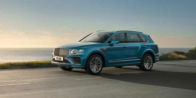 Bentley Monaco Bentley Bentayga Azure SUV in Topaz blue paint driving dynamically by the ocean with 22 inch 10 spoke directional wheels