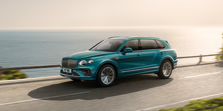 Bentley Monaco Bentley Bentayga Extended Wheelbase Azure SUV in Topaz blue paint driving dynamically by the ocean