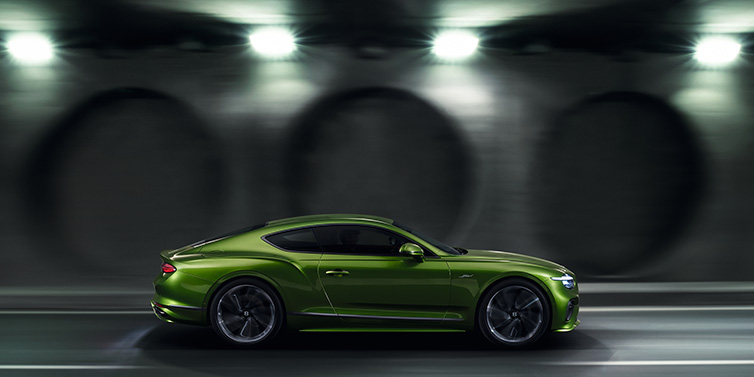 Bentley Monaco Bentley Continental GT Speed coupe profile in Tourmaline Green driving dynamically past a concrete wall at night