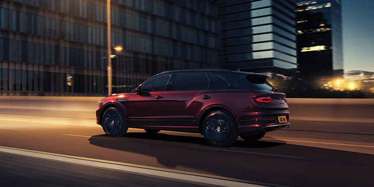 Bentley Monaco Bentley Bentayga Extended Wheelbase Mulliner SUV in Cricket Ball red paint driving dynamically in city at night