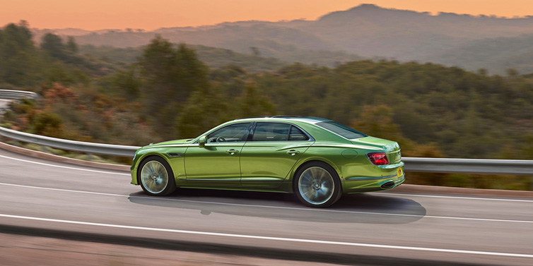 Bentley Monaco Bentley Flying Spur Speed sedan side profile in Tourmaline Green paint driving dynamically on a mountain road at sunset