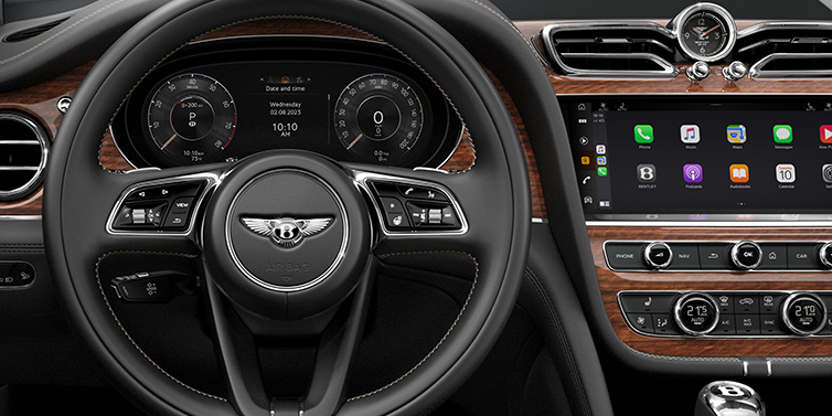 Bentley Monaco Bentley Bentayga SUV front interior detail of steering wheel and driver screens surrounded by Beluga black hide and Crown Cut Walnut veneer