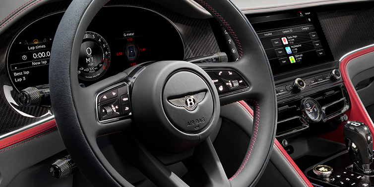 Bentley Monaco Bentley Flying Spur Speed sedan front interior detail showing steering wheel and driver screens surrounded with Hotspur red and Gravity Grey hides